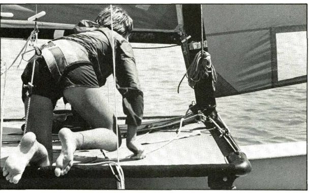 Black and white photo of a crew kneeling on a Hobie trampoline by the mast with the jib sheet in hand