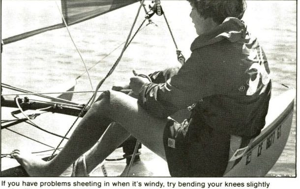 Black and white photo of a crew sitting on the side rail of a Hobie pulling the jib sheet with bent knees