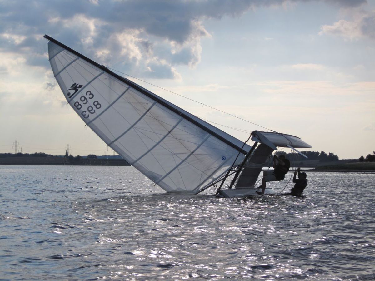 Two sailors righting a capsized Hobie Cat with a righting line, the mast lying flat on the water