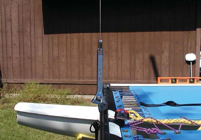 A crescent wrench hanging as a plumb weight from a Hobie 14 main halyard beside the mast base, with a carpenter level on the trampoline